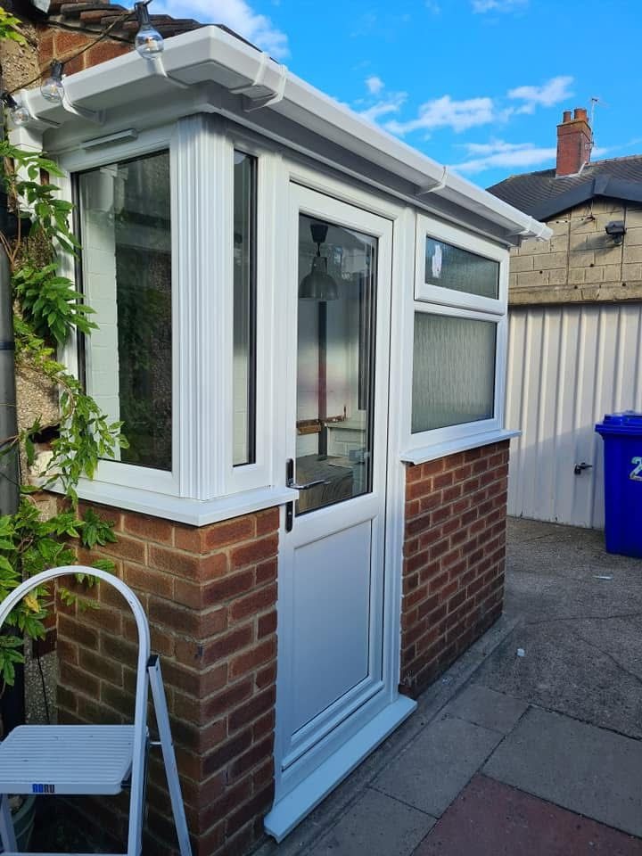 Corner view of a new white uPVC porch infill with composite door on a brick base