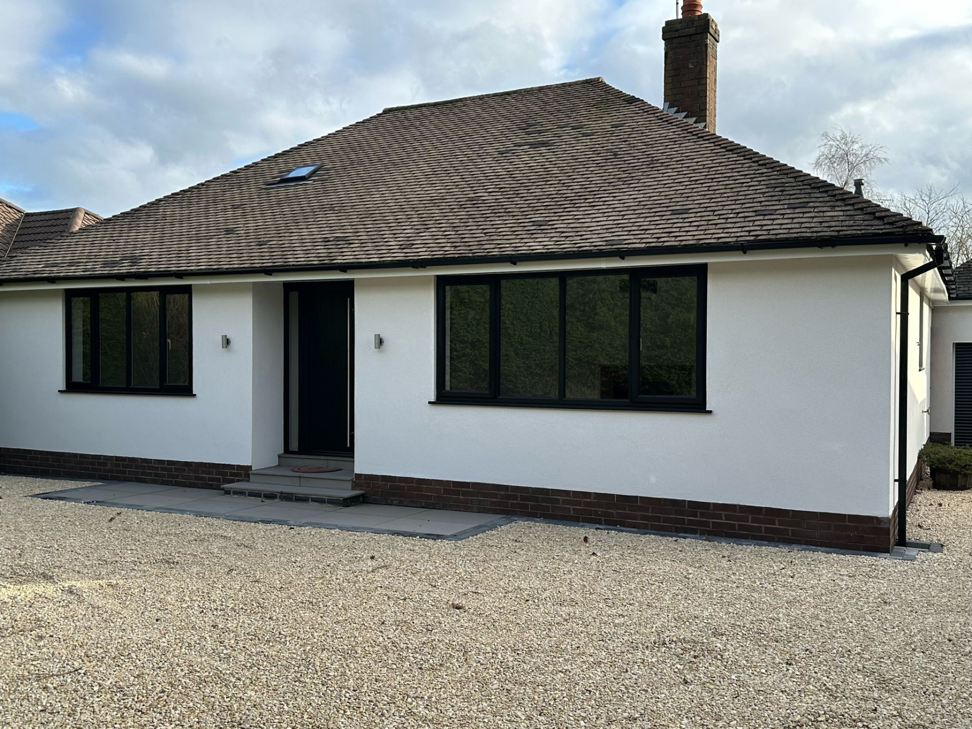 White rendered bungalow fitted with large black uPVC replacement windows and matching door